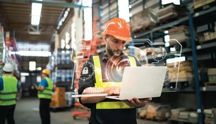 A procurement professional using a laptop in a warehouse to manage what is supplier onboarding digital workflows.
